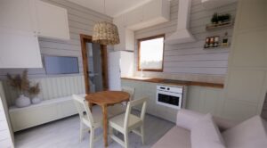 Kiełpino - Nowoczesny domek modułowy z jasnym wnętrzem, wyposażony w funkcjonalną kuchnię, stół i krzesła. Idealny jako domek mobilny na wakacje lub całoroczny dom mobilny. Przykład stylowego i praktycznego designu w domach modułowych.