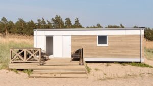 Mścice - Domek mobilny z drewnianą elewacją i tarasem na plaży, w tle drzewa i trawy.